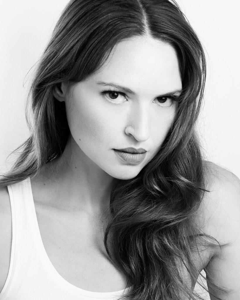 Black-and-white beauty portrait of model Bibi Alfonso with long wavy hair and a white top against a light background.