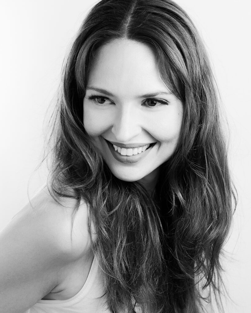 Black-and-white portrait of model Bibi Alfonso smiling with long, voluminous hair against a light background.