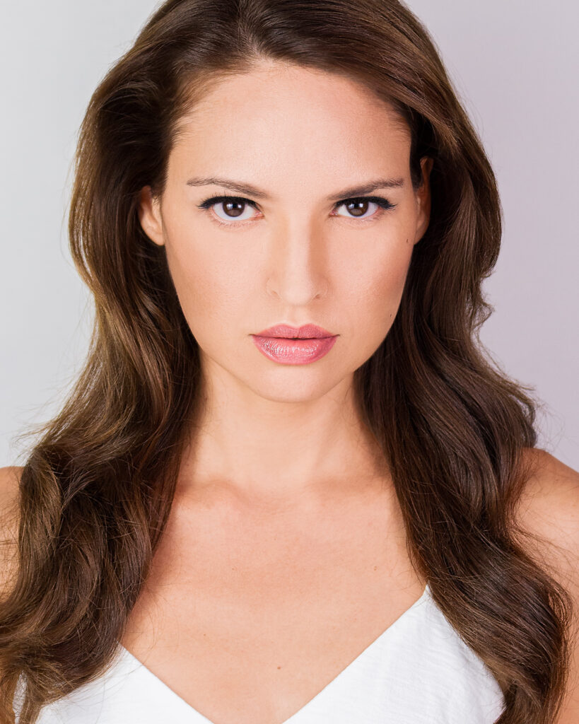 Model Bibi Alfonso in a close-up portrait with long brown hair and natural makeup against a light background.