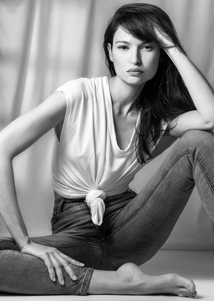 Model Bibi Alfonso seated in jeans and a white knotted T-shirt in a black-and-white portrait.